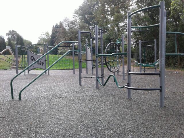 Multi-play unit including spinning poles, climbing walls, netted climbing ropes and metal ladders situated on grass