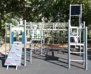 Multi-play unit including climbing board, netted climbing bridge, sliding pole, metal ladders and chained on balance bridge situated on wetpour