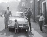 Old image of a family stood by a car